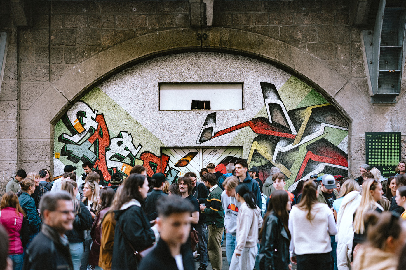 Besucher:innen spazieren entlang der Bogenmeile vor bemalter Fassade beim Bogenfest